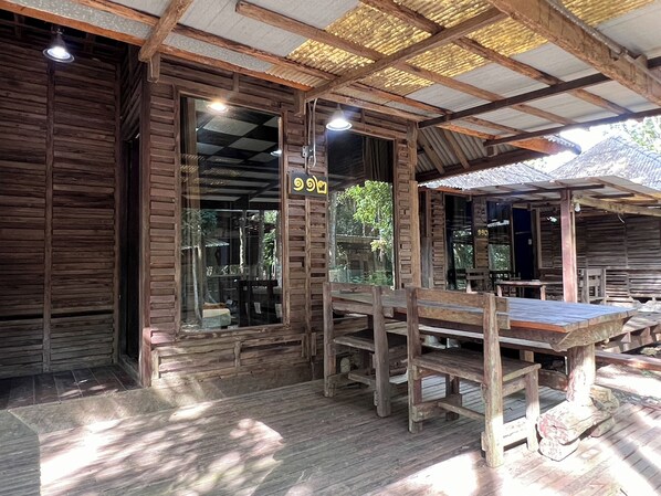 A rustic wooden building with a large window and a wooden table and bench set up outside.