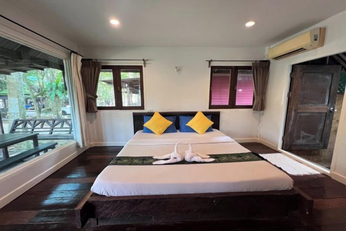A hotel room with a large bed, two windows, and a view of the outdoors.