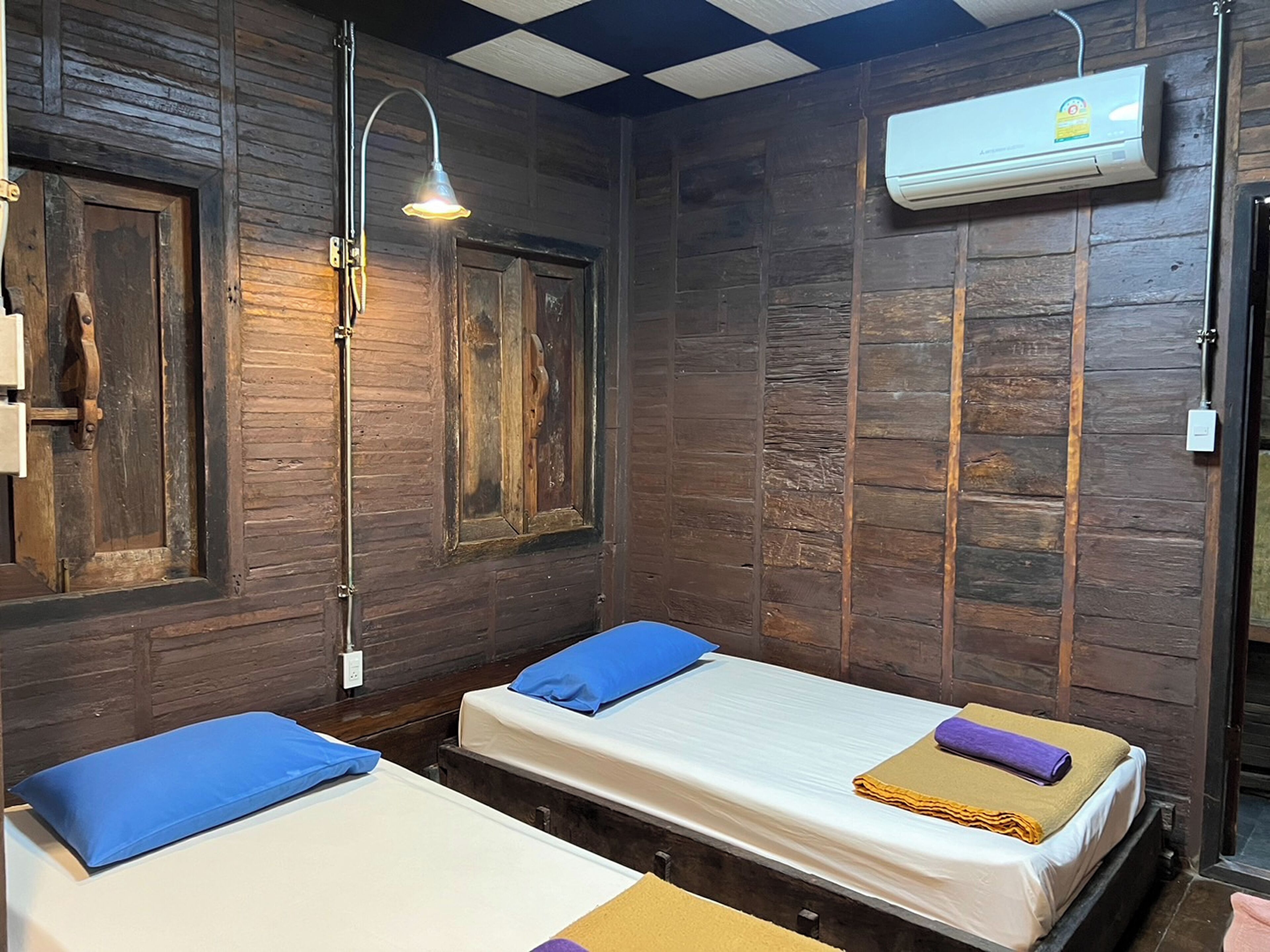 A room with two beds, wooden walls, a ceiling fan, and an air conditioning unit.