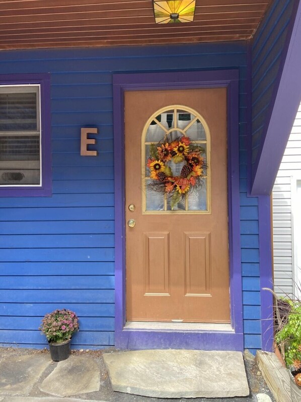 Une maison à l’extérieur bleu, avec une porte d’entrée marron et une guirlande accrochée à la porte.