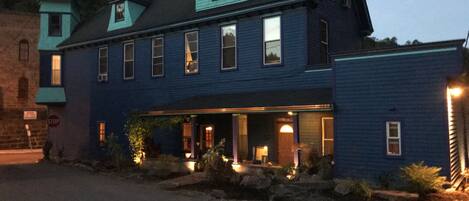 A two-story building with a dark blue exterior, a gabled roof, and a porch area with lights.