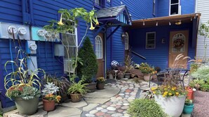 A blue house with a stone-paved front yard and various potted plants.