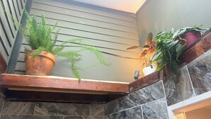 A staircase with a wooden handrail, a potted plant on the landing, and a stone wall.