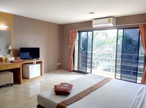 A hotel room with a bed, a desk with a television, a small refrigerator, and a window with curtains.