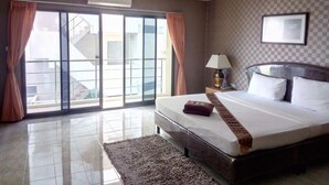 A hotel room with a large bed, a nightstand with a lamp, a window with curtains, and a view of the outside. - Pearl Place Hotel (Hat Yai)