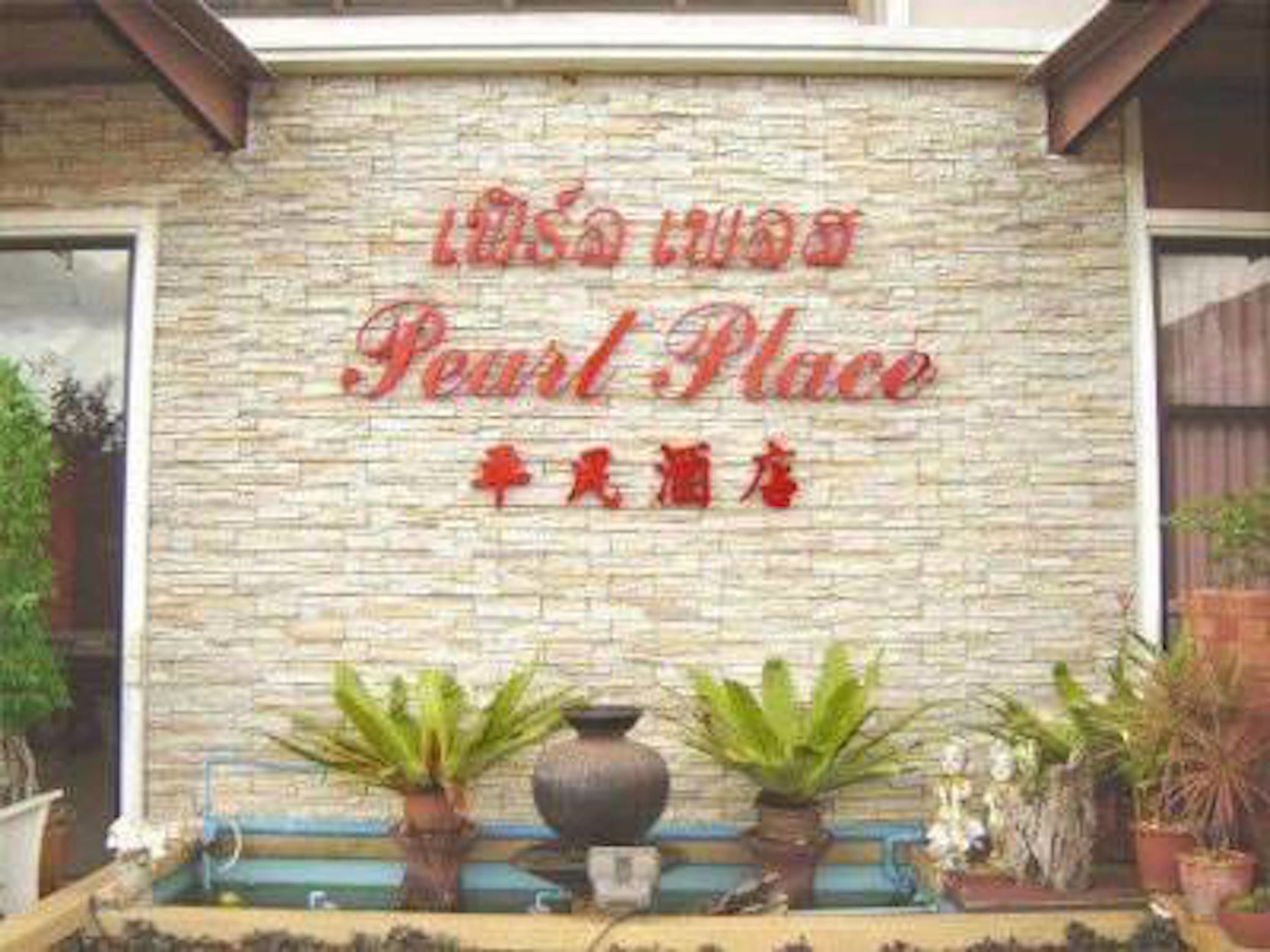 A stone wall with 'Pearl Place' and 'Siam Hotel' signage. There are potted plants in front.