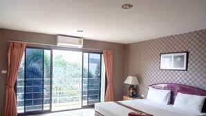A hotel room with a large bed, a nightstand, a lamp, and a view of palm trees through a sliding glass door. - Pearl Place Hotel (Hat Yai)