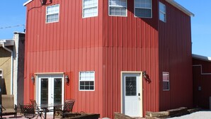 A red two-story building with a white door and windows, a satellite dish, and outdoor furniture.