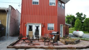 A red metal building with a patio area featuring a table, chairs, and a grill.