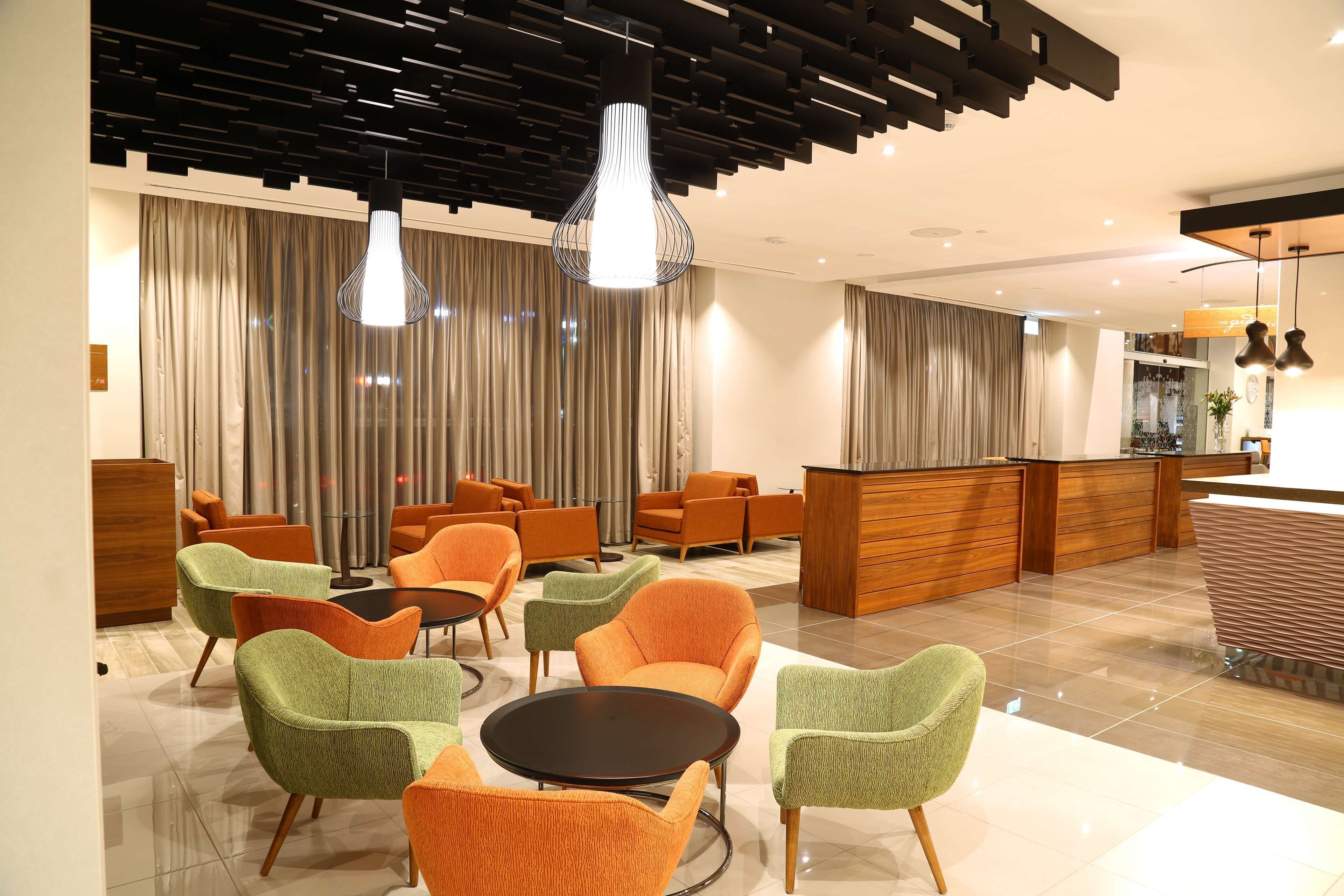A modern hotel lobby with a reception desk, seating area with chairs, and a large window with curtains.