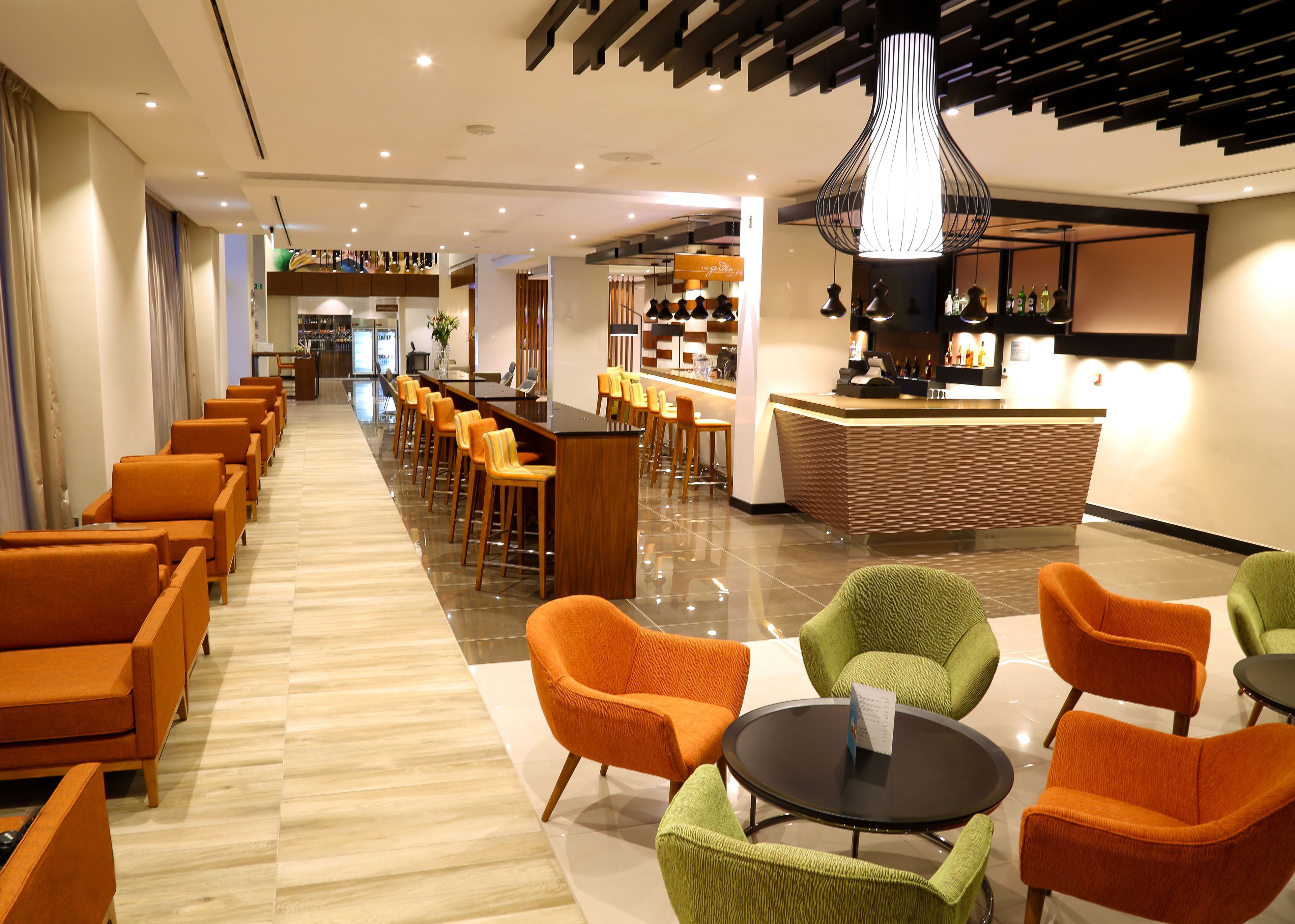 A hotel lobby with a long row of orange chairs, a reception desk, and a bar area.