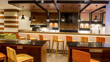 Un espace bar moderne avec des comptoirs en bois, des chaises orange et une variété de bouteilles d’alcool exposées sur des étagères.