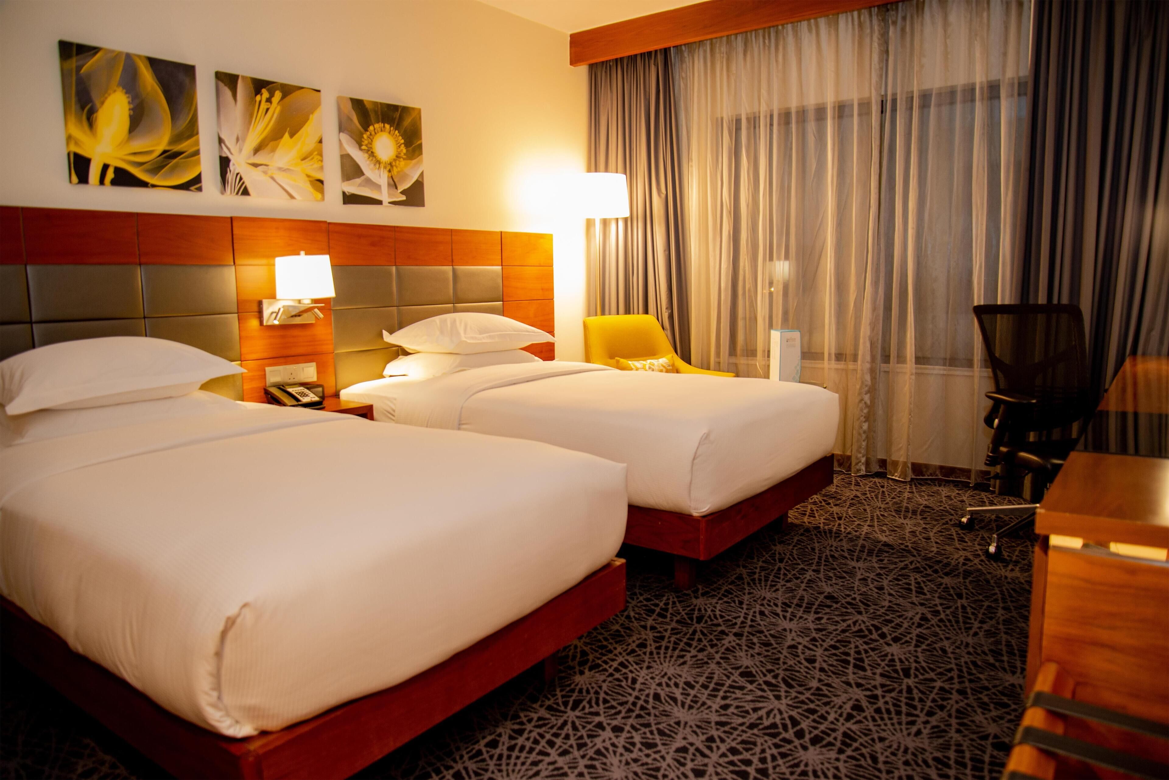 Una habitación de hotel con dos camas, una mesita de noche, una lámpara, una silla y un escritorio.
