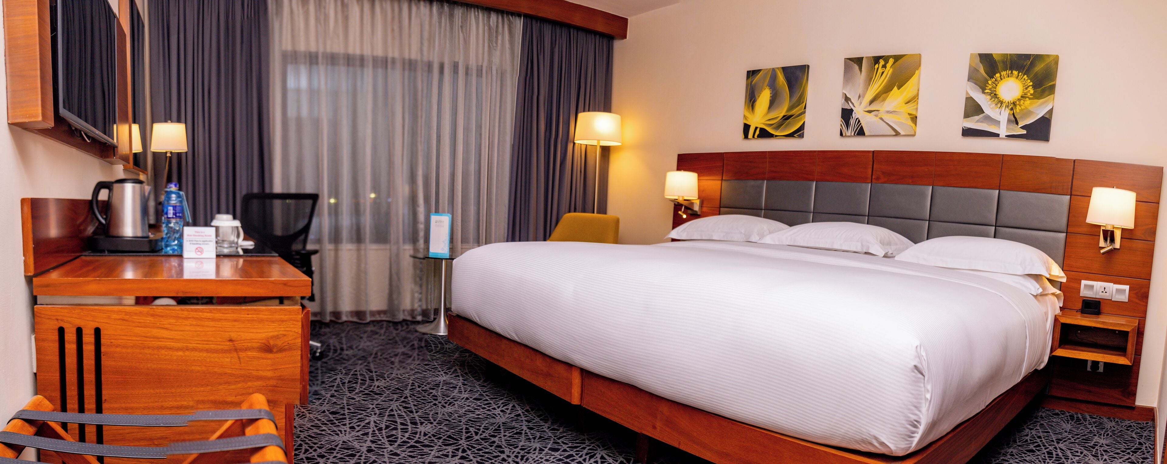 A hotel room with a large bed, a desk with a chair, a coffee maker, and two wall-mounted lamps.