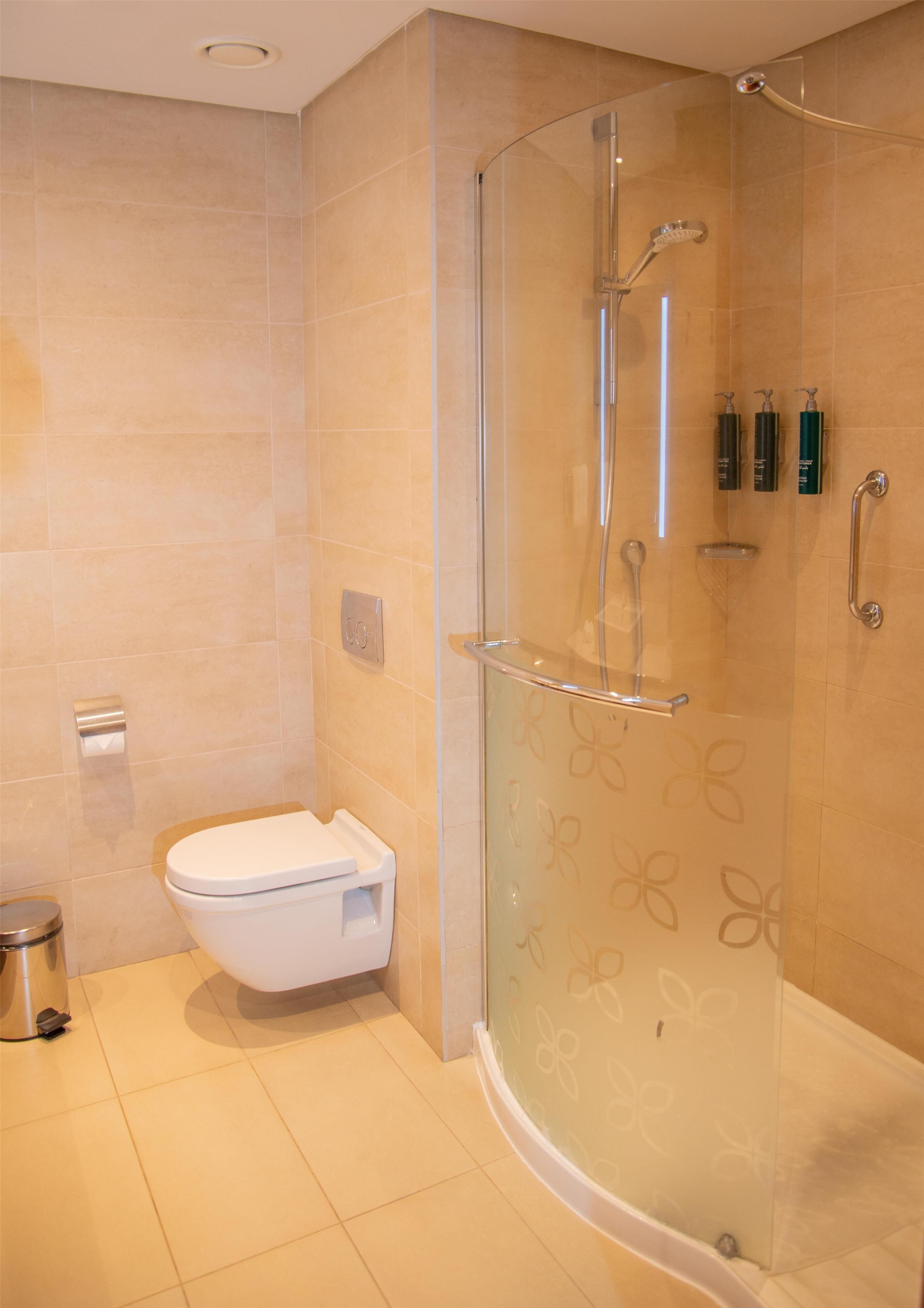 A modern bathroom with a glass-enclosed shower, a toilet, and a trash can.