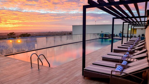 Zona de piscina en la azotea con sillones de descanso y vistas a la ciudad al atardecer.