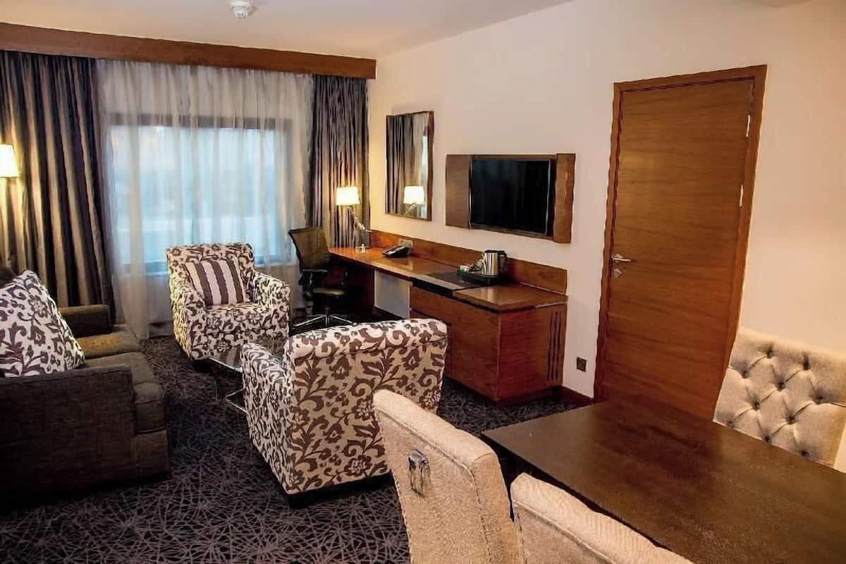 A hotel room with a sofa set, a desk with a lamp, a television, and a door.