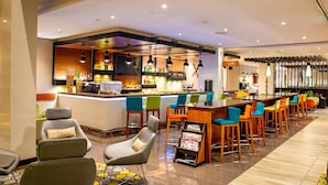 Un área de bar moderna con barra, varios taburetes y un espacio de asientos con sillas.