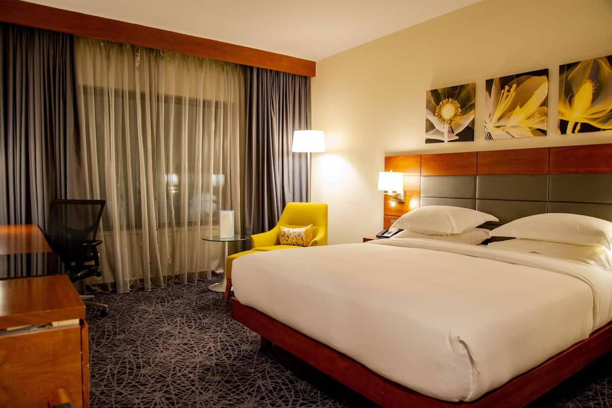 A hotel room with a large bed, a desk, a chair, and a lamp.