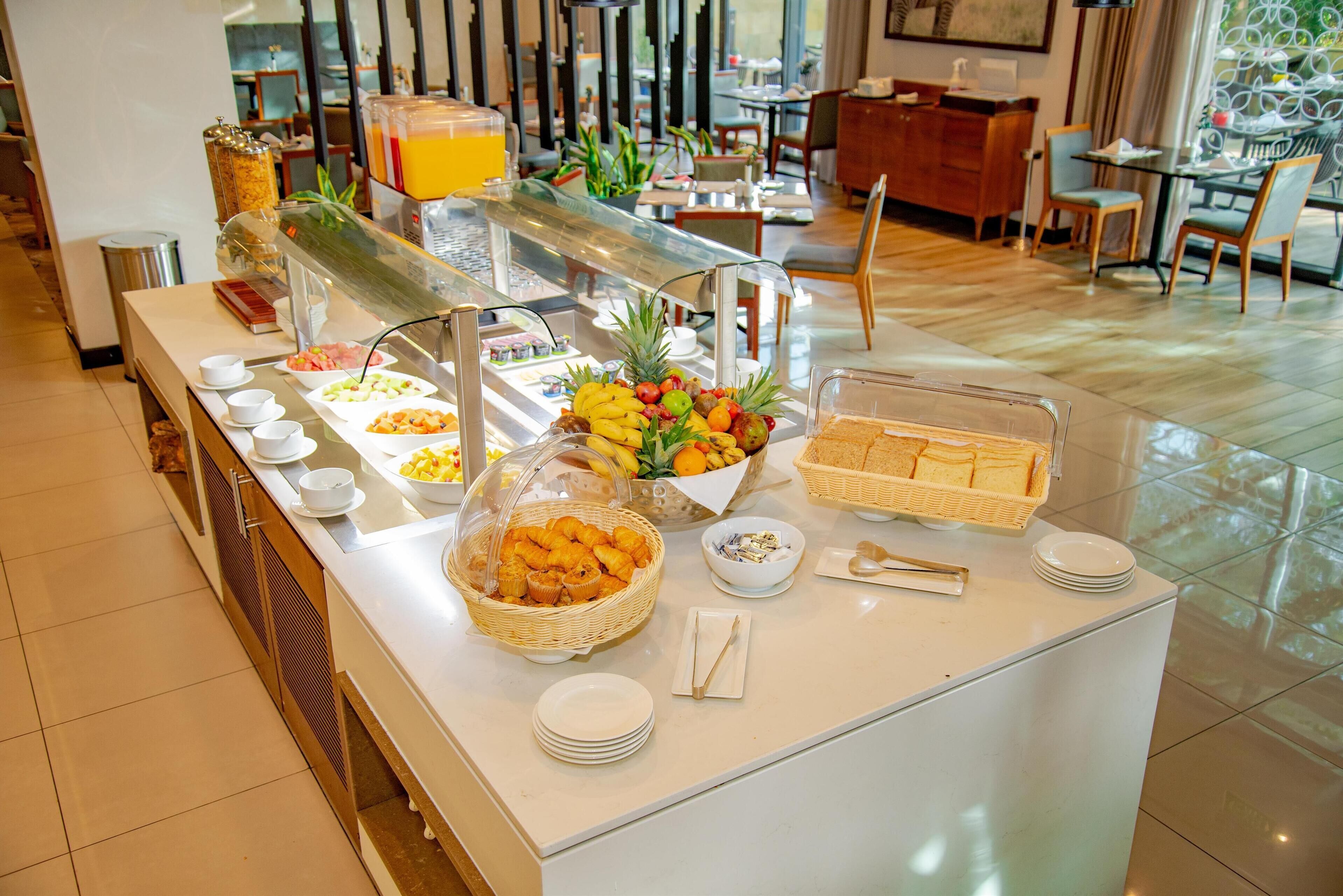 A buffet setup with various food items, a juice dispenser, and a seating area in the background.