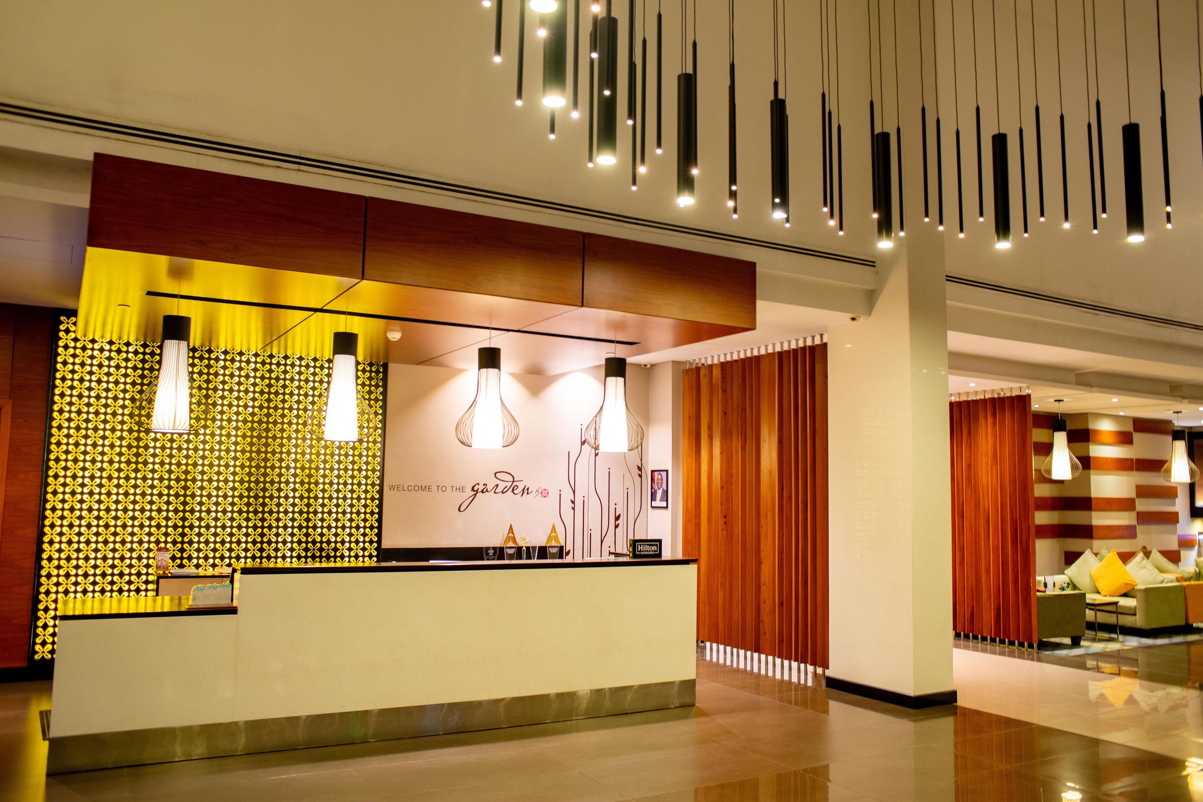 A hotel reception area with a modern design, featuring a reception desk, decorative wall panels, and hanging pendant lights.