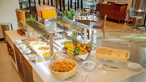 Un bufé con diversas opciones de comida, entre ellas frutas, pasteles y pan.