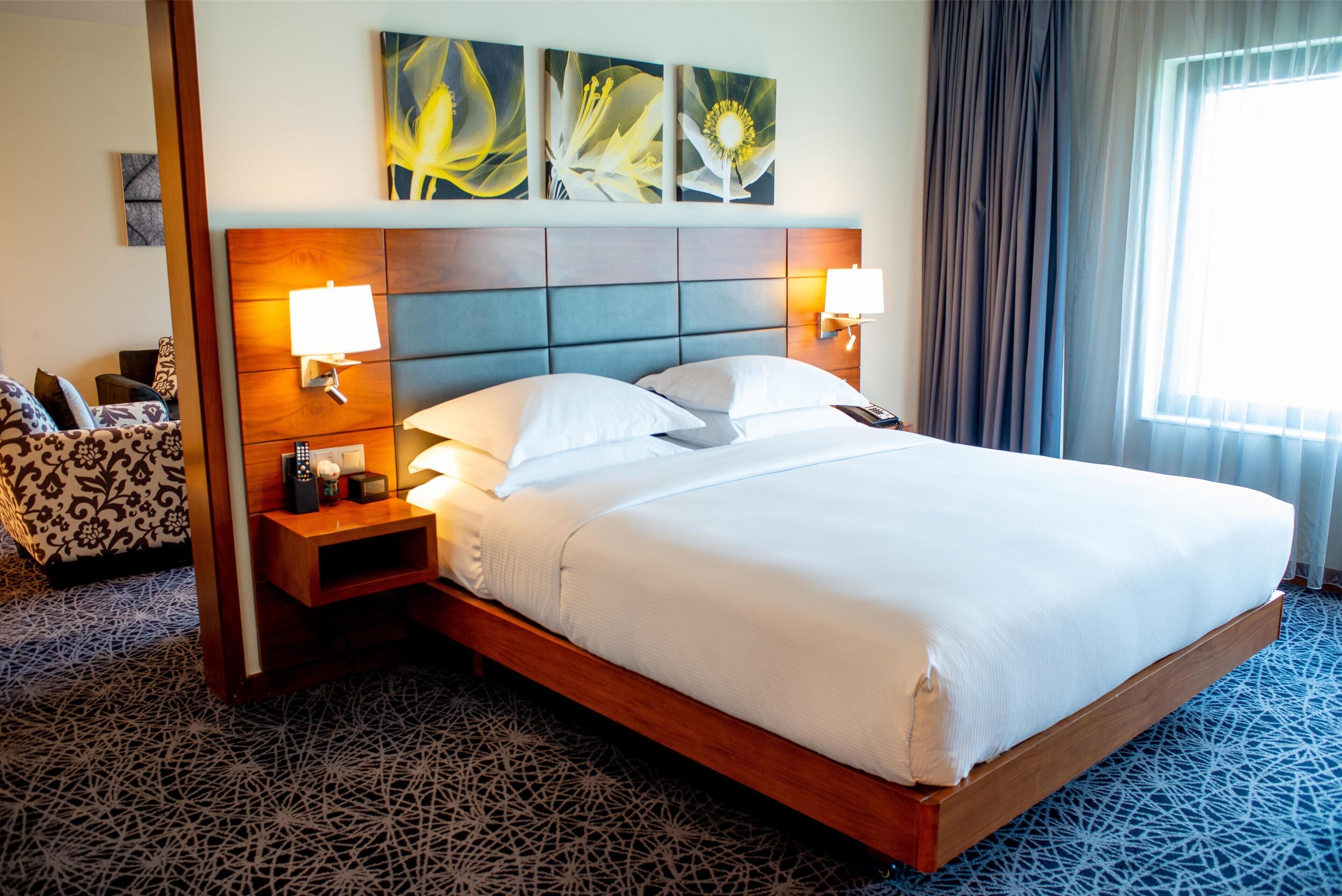 Ein Hotelzimmer mit einem großen Bett, zwei Nachttischen mit Lampen, einem Kopfteil und einem floralen Bild über dem Bett.