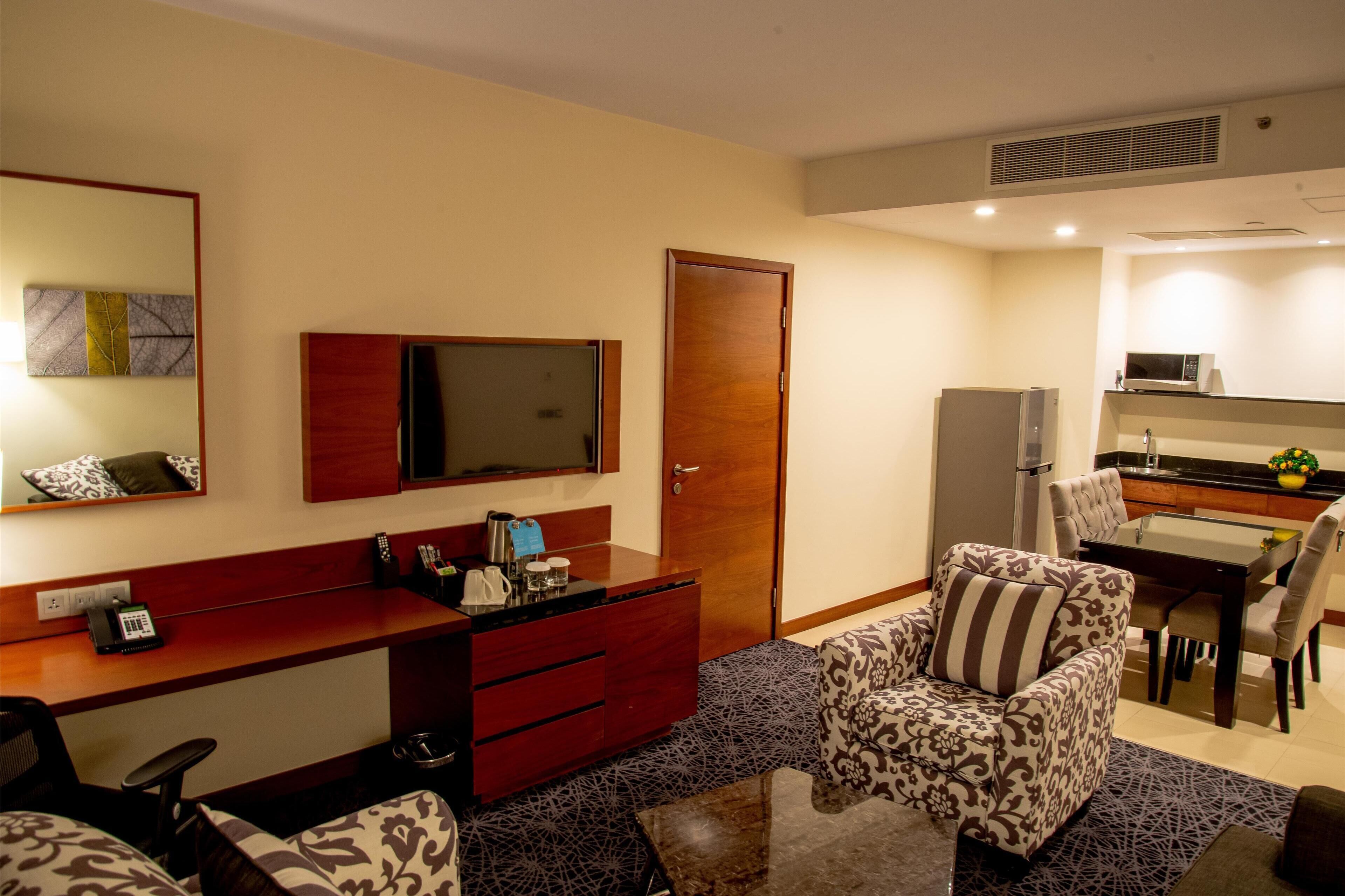 Une chambre d’hôtel compacte comprenant un coin cuisine, un espace repas, un canapé et un bureau avec un miroir et un téléphone.