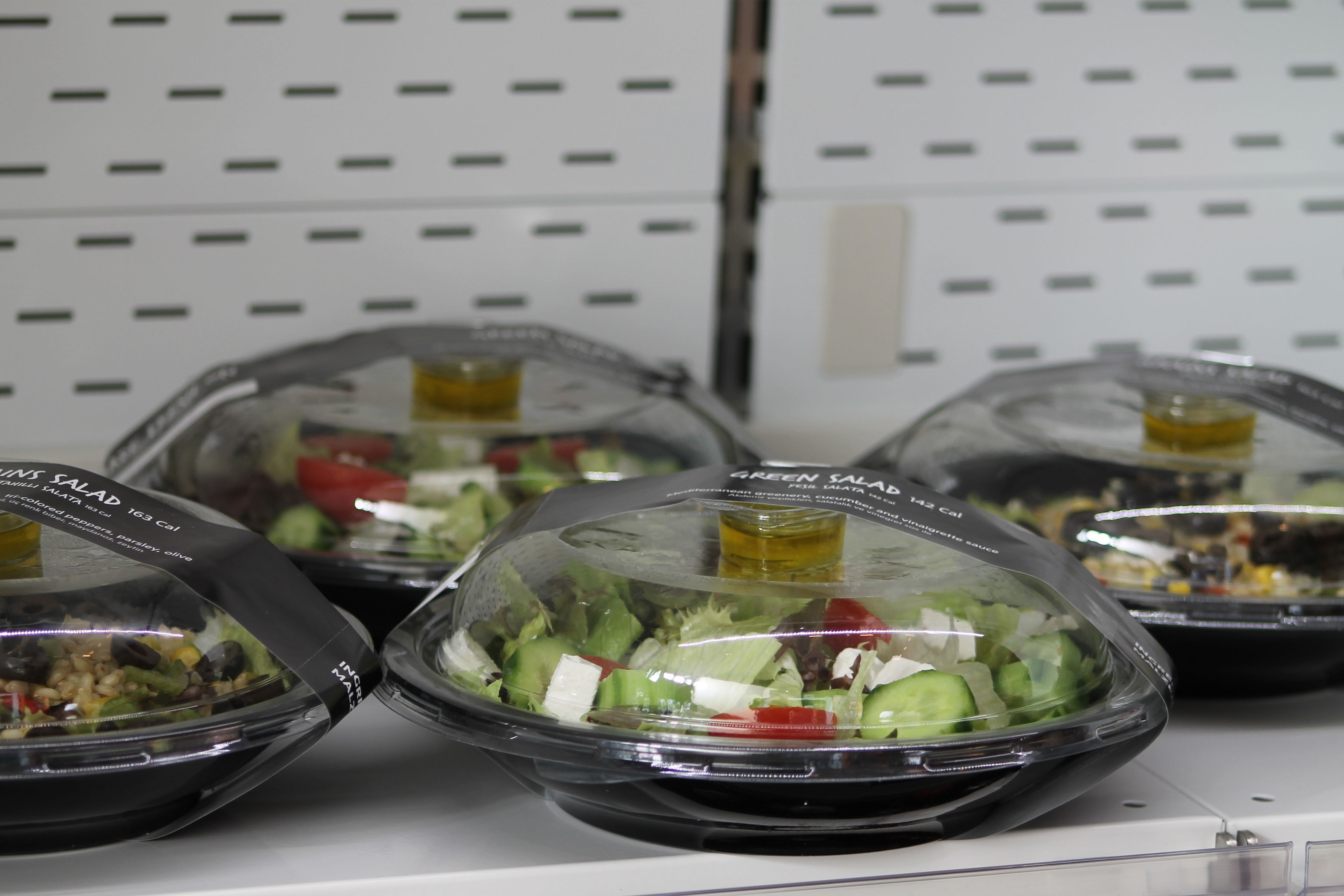 Salad bowls on a shelf with labels indicating different types of salads.