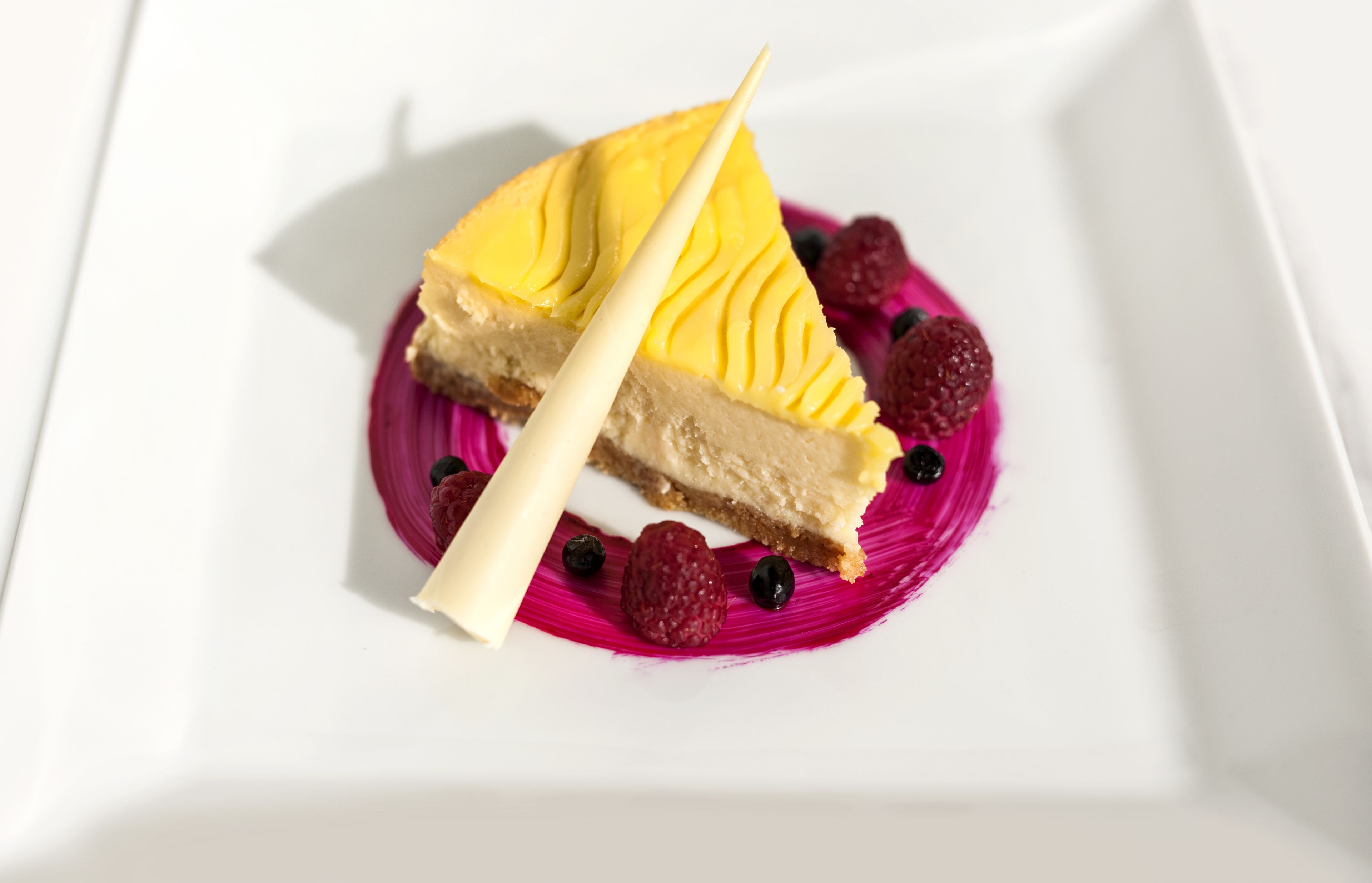 Une part de gâteau au fromage, décorée de motifs et d’éléments de présentation, servie sur une assiette blanche.