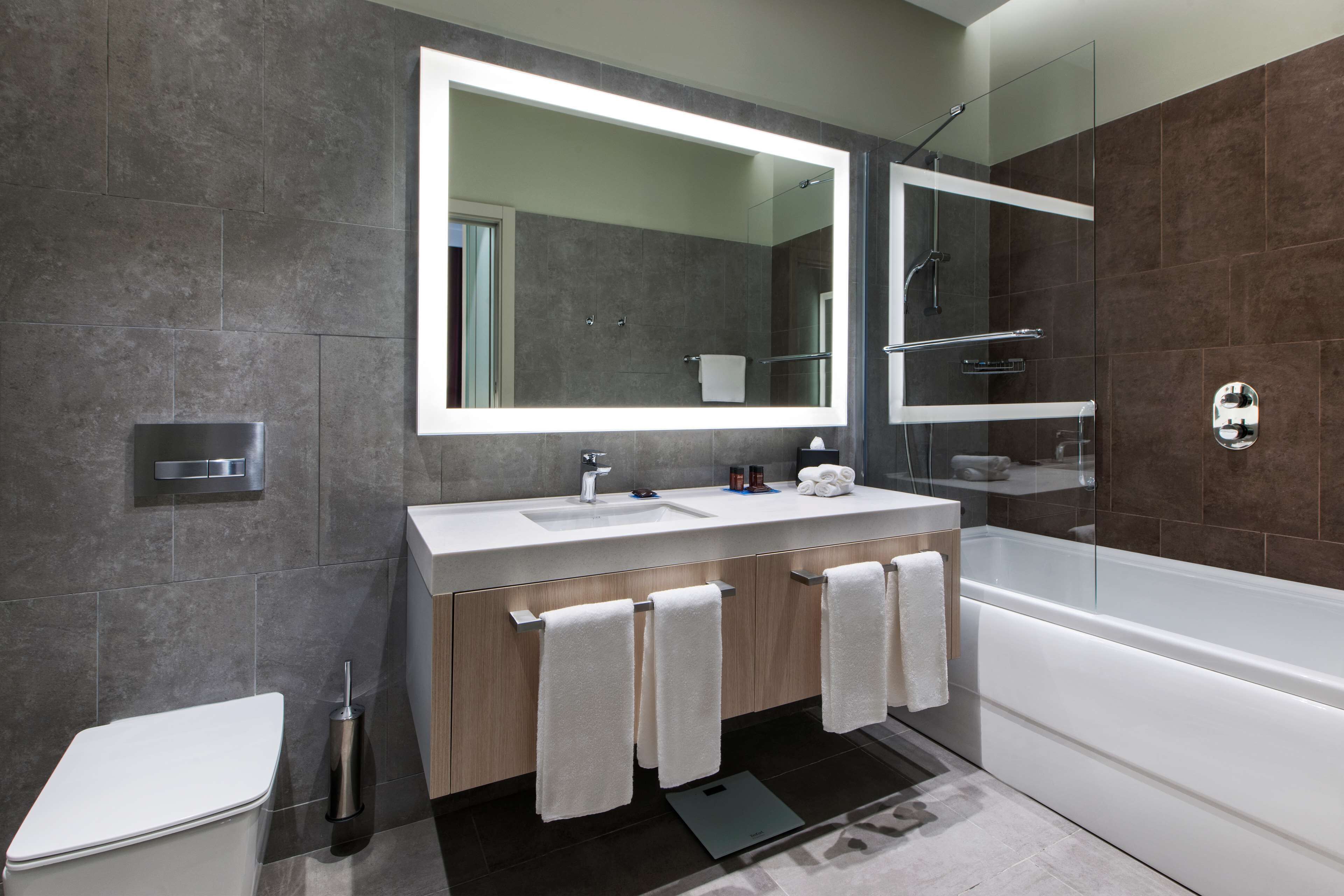 Un baño moderno con un espejo grande, un lavamanos, un inodoro y una bañera.