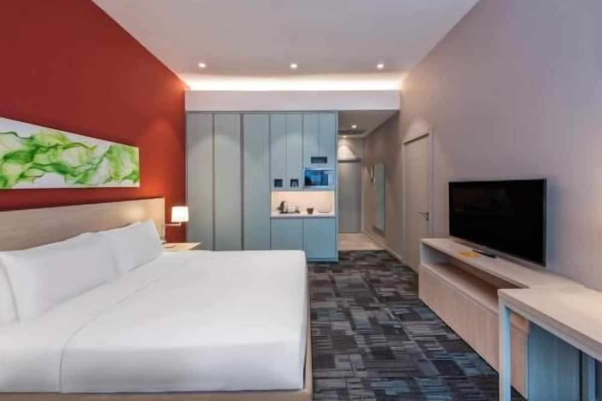 A hotel room with a bed, a TV, a painting, and a kitchenette.