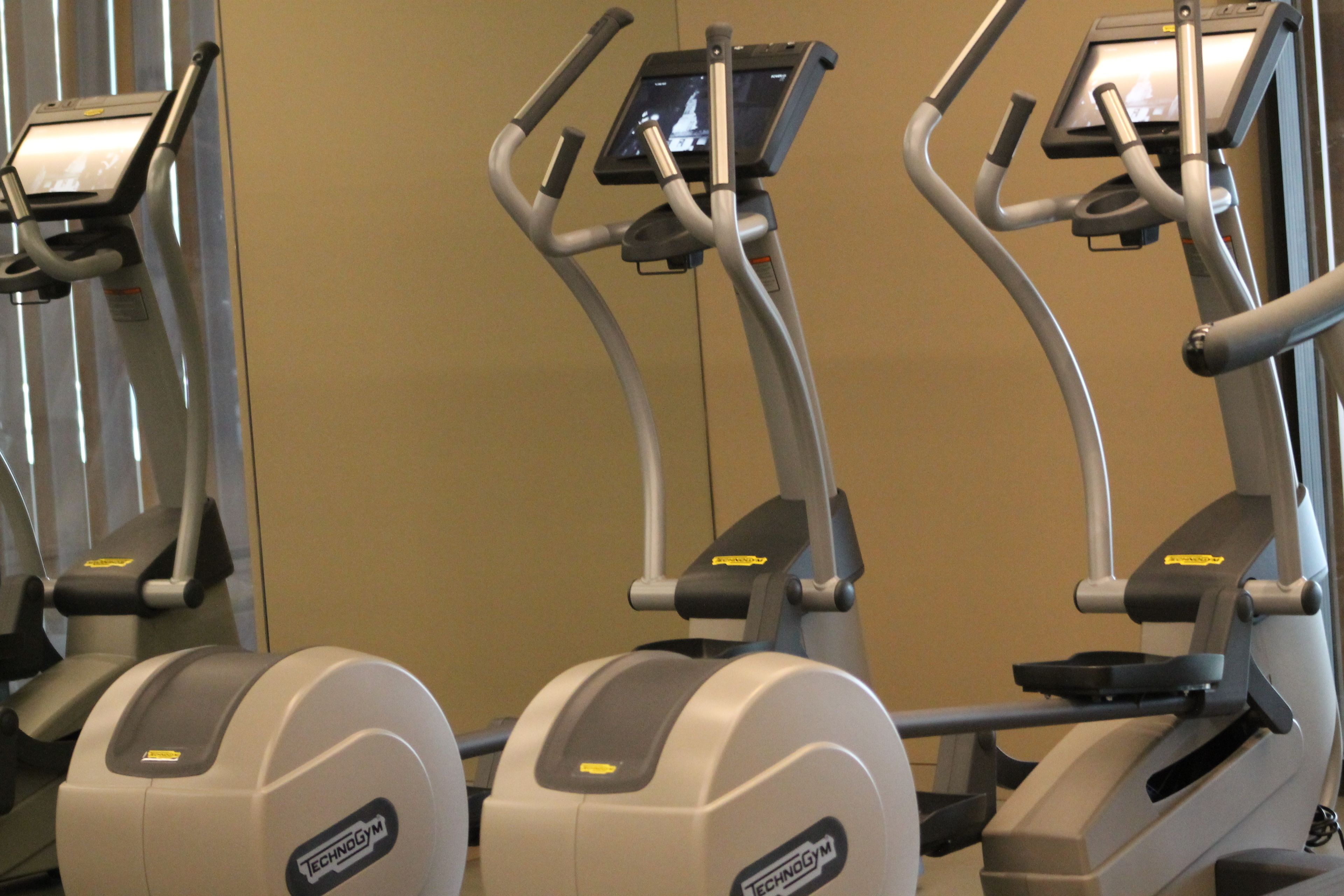 Three exercise machines with digital displays, positioned against a plain wall.