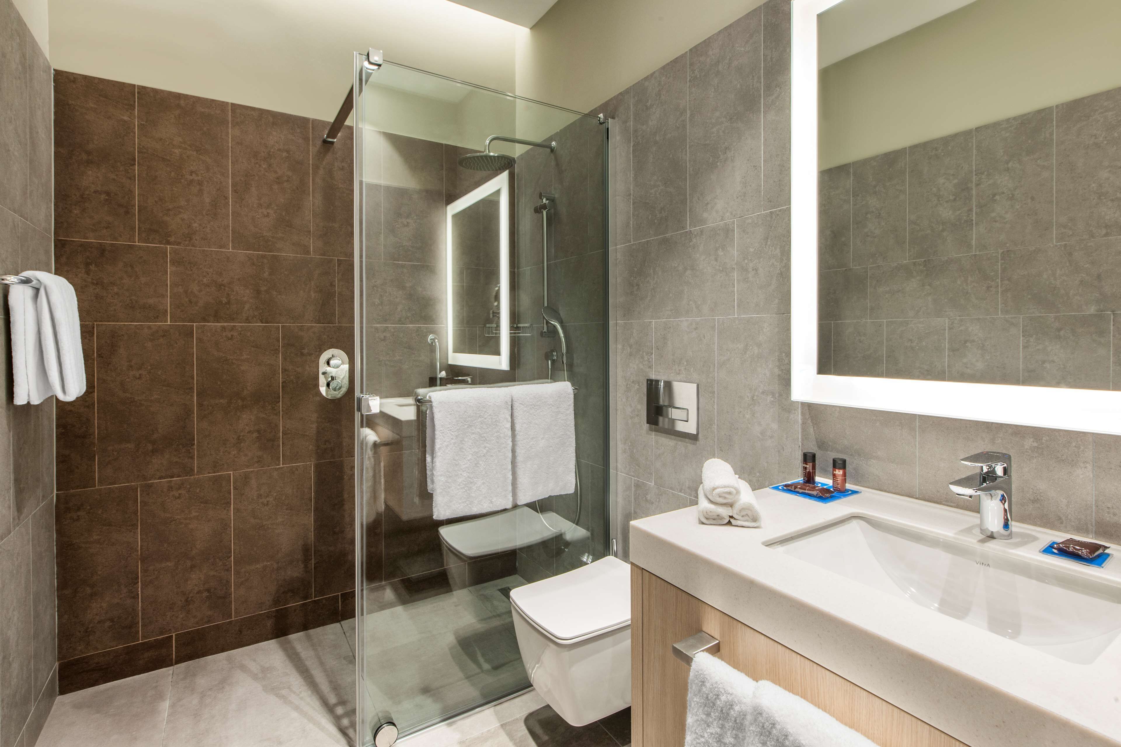 Un baño moderno con cabina de ducha de vidrio, un espejo grande y un lavabo blanco con tocador.