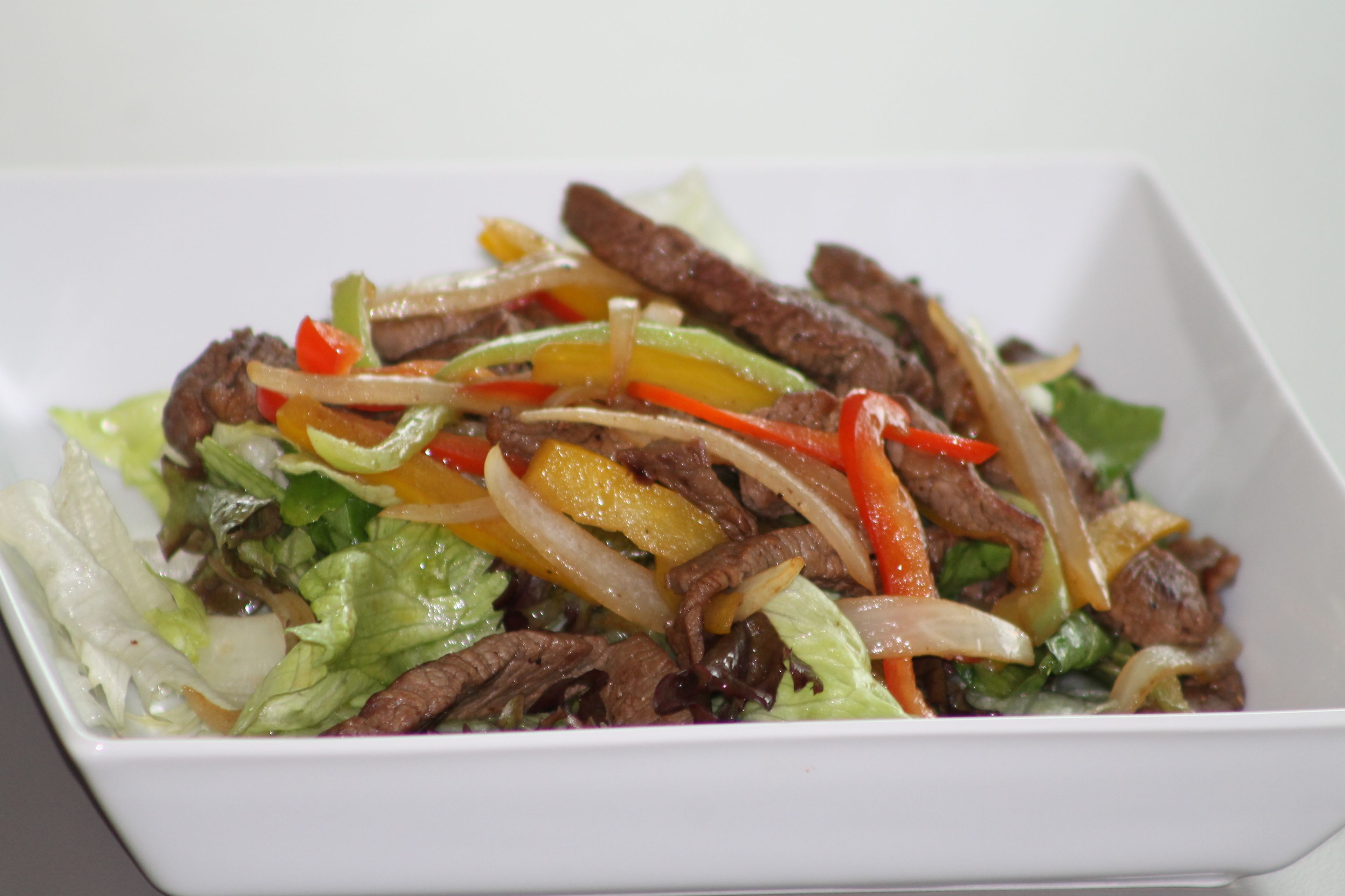 Une assiette carrée blanche contenant un plat de bœuf et de légumes sautés.