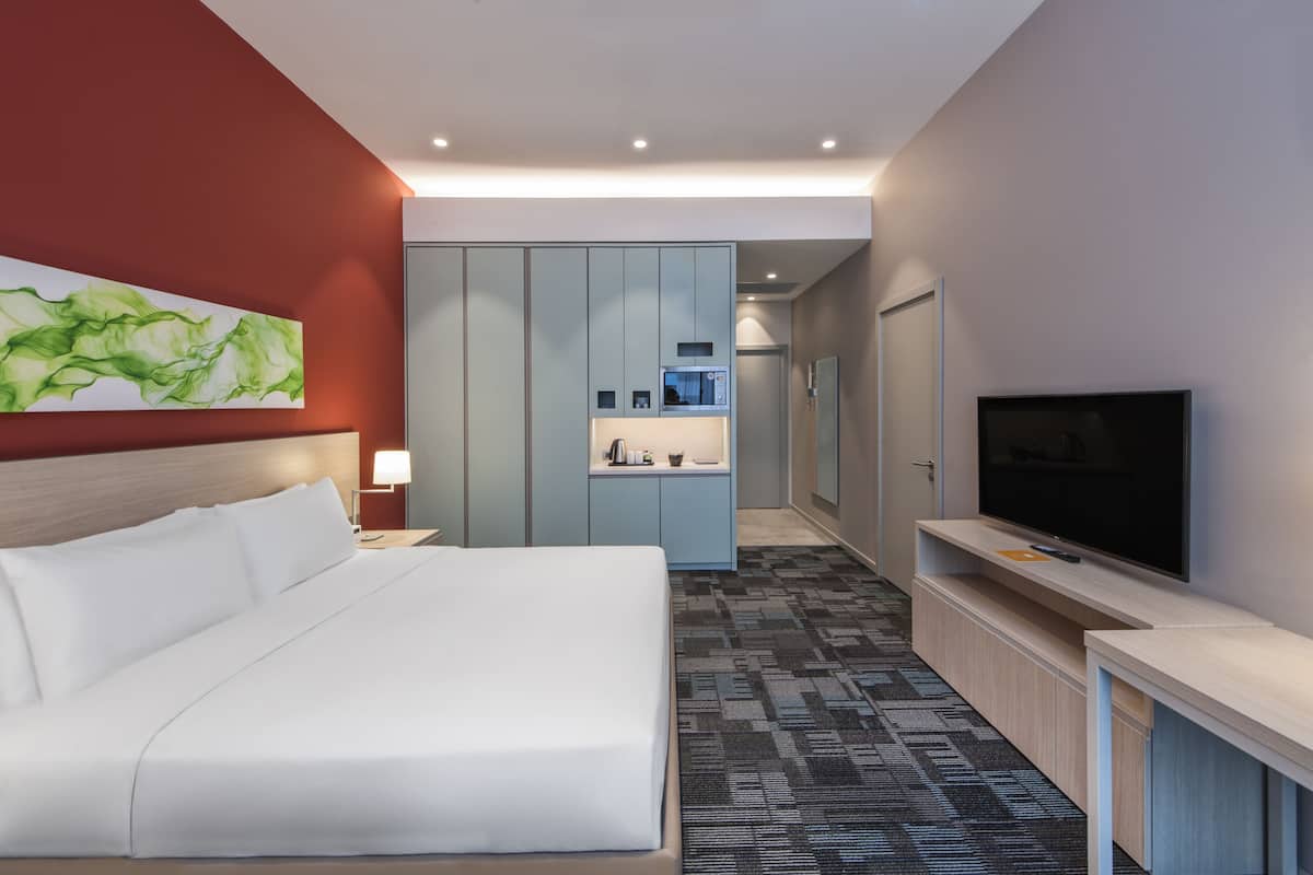 A modern hotel room with a large bed, a television, a minibar, and a bathroom visible through a door.
