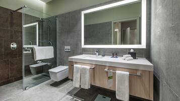 Un baño moderno con ducha acristalada, un espejo grande y un tocador con lavamanos y toallero.