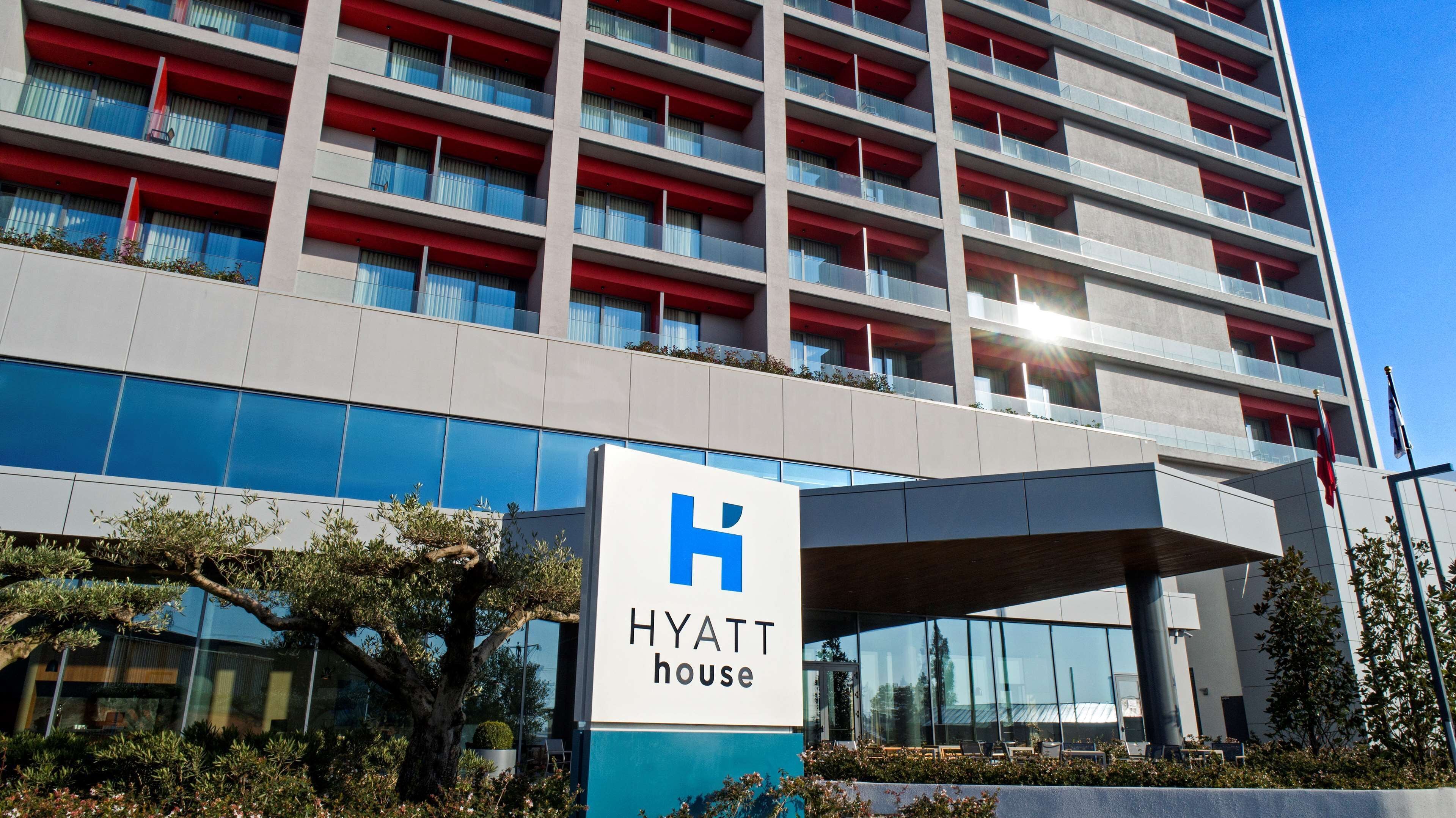 Un moderno edificio de hotel con un llamativo letrero de 'Hyatt House', amplias ventanas y fachada en rojo y gris.