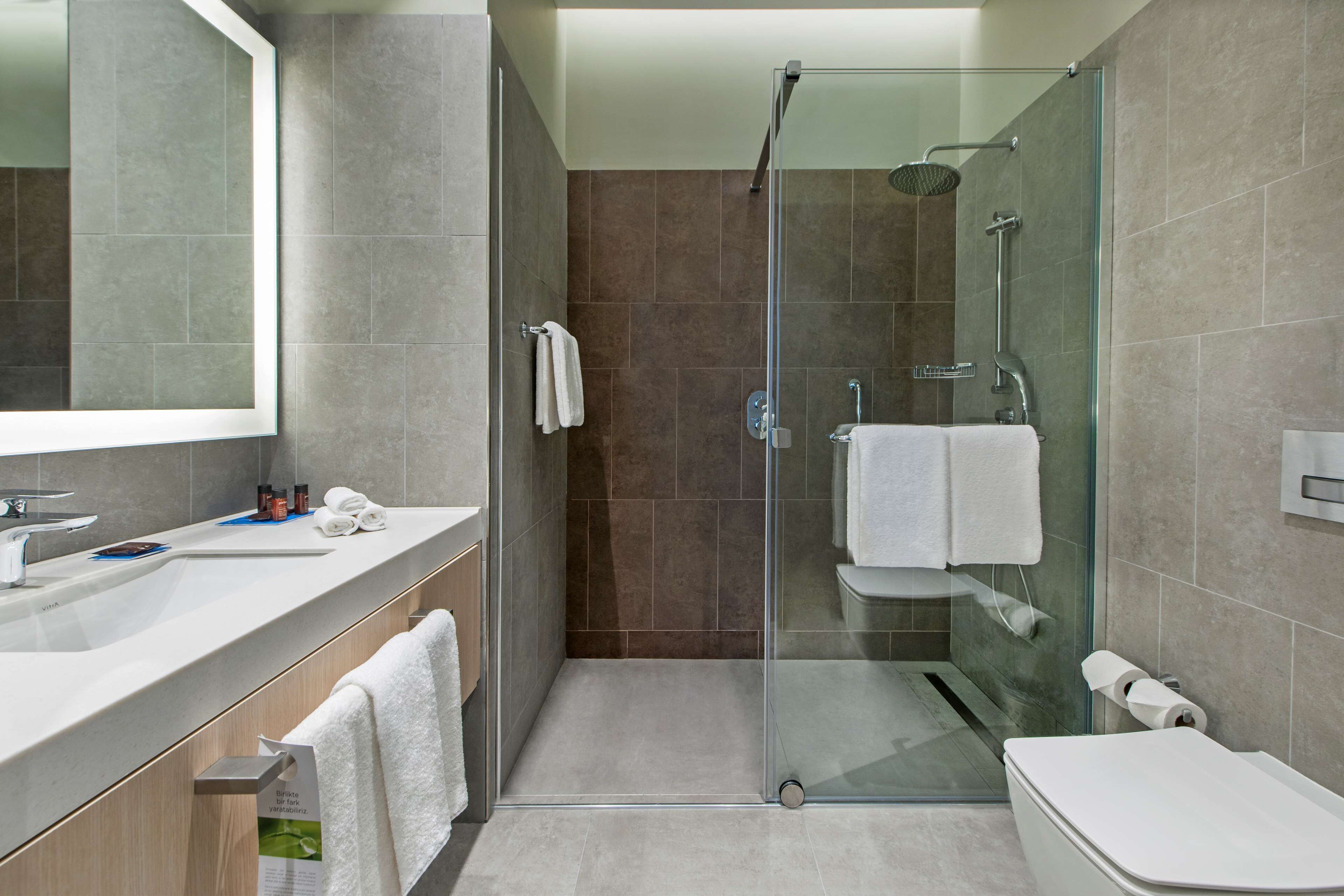 Un baño moderno con ducha envuelta en vidrio, un espejo grande y un lavamanos blanco.