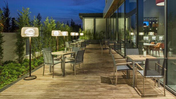 An outdoor dining area with tables and chairs, surrounded by glass walls and a wooden deck. - Hyatt House Gebze (Gebze)