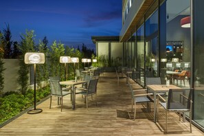 An outdoor dining area with tables and chairs, surrounded by glass walls and a wooden deck. - Hyatt House Gebze (Gebze)
