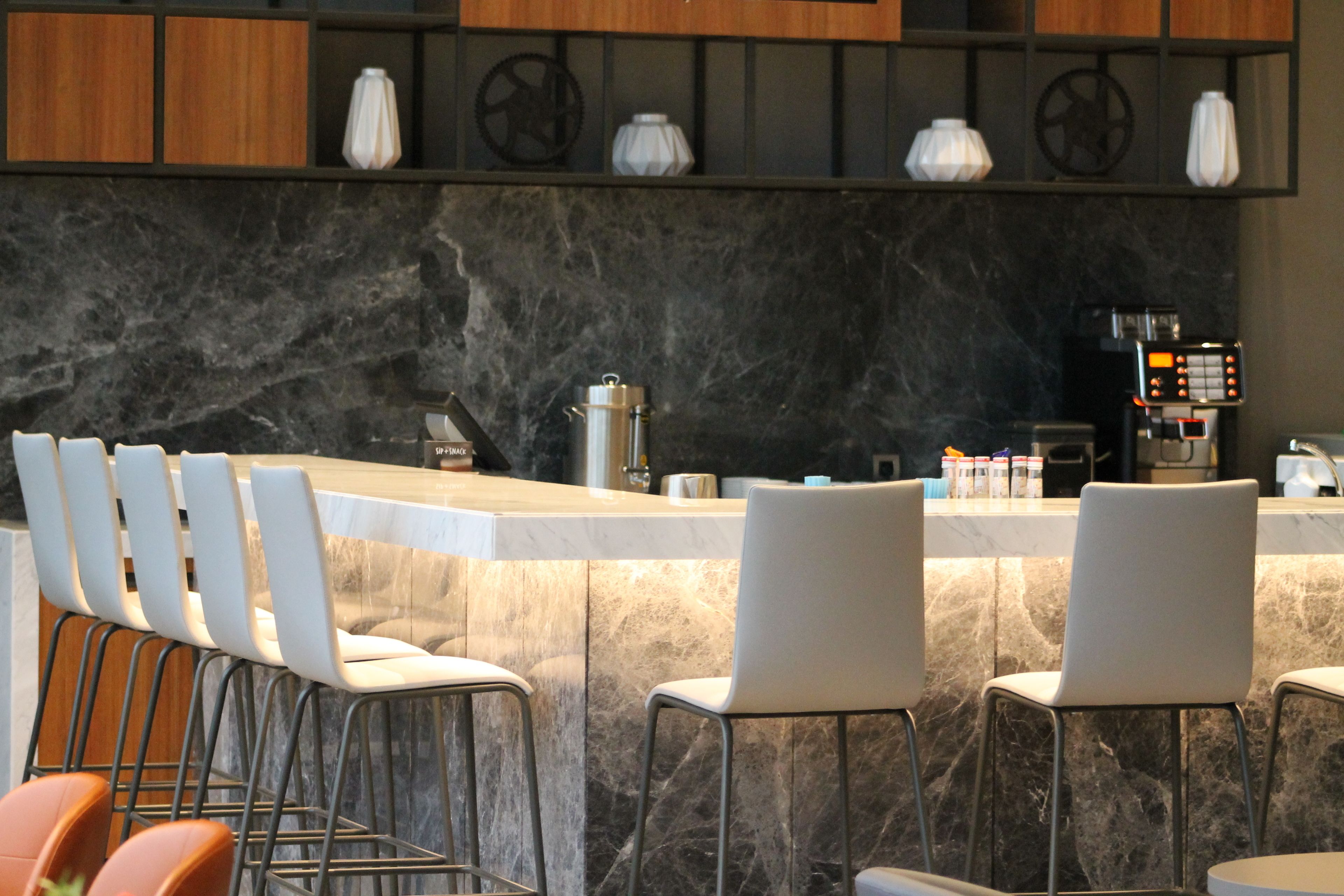 A modern bar area with a marble countertop, bar stools, and a coffee machine.