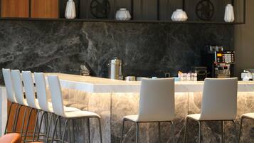 Zona de bar moderna con encimera de mármol, taburetes y una máquina de café.