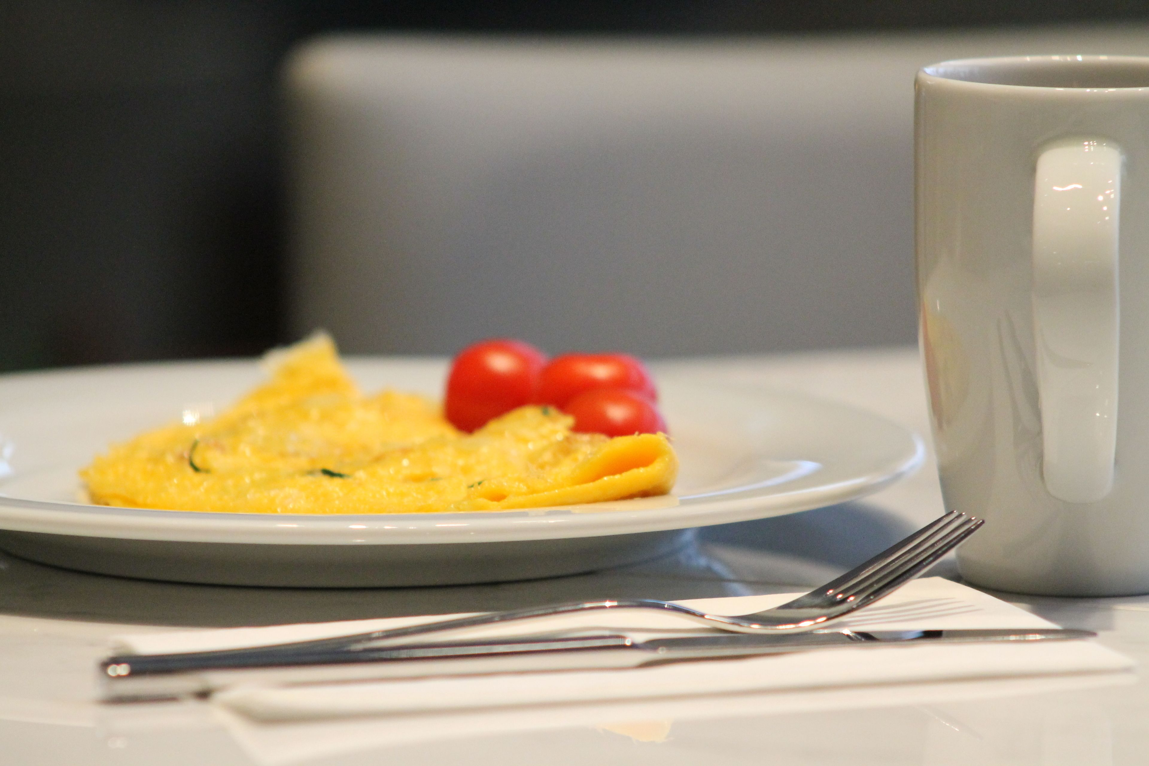 A plate with an omelette and cherry tomatoes, a white mug, and a fork on a table.