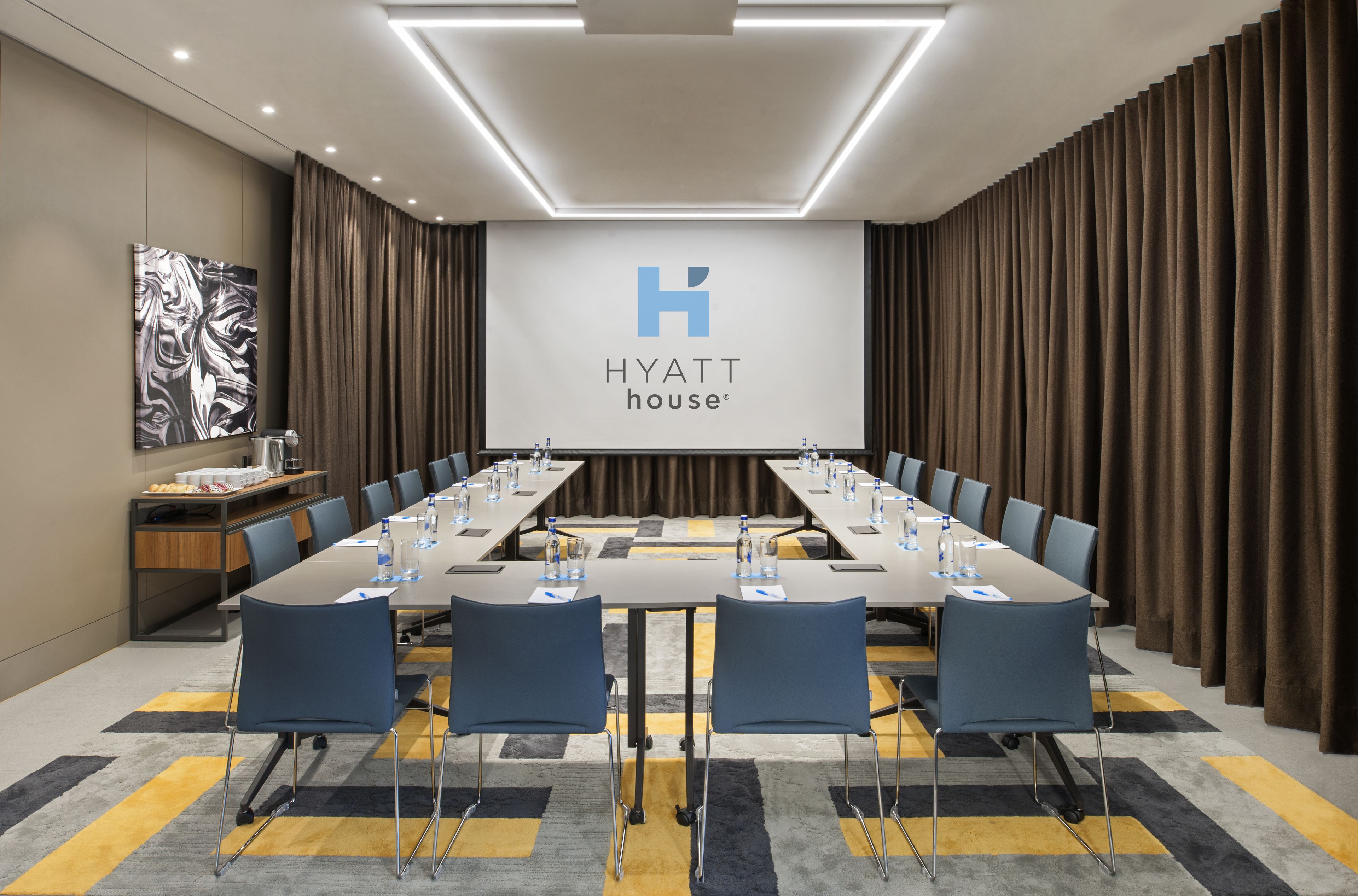 A conference room with a long table, chairs, and a large screen displaying the Hyatt House logo.