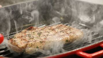 A steak being grilled on a red grill pan with visible smoke.