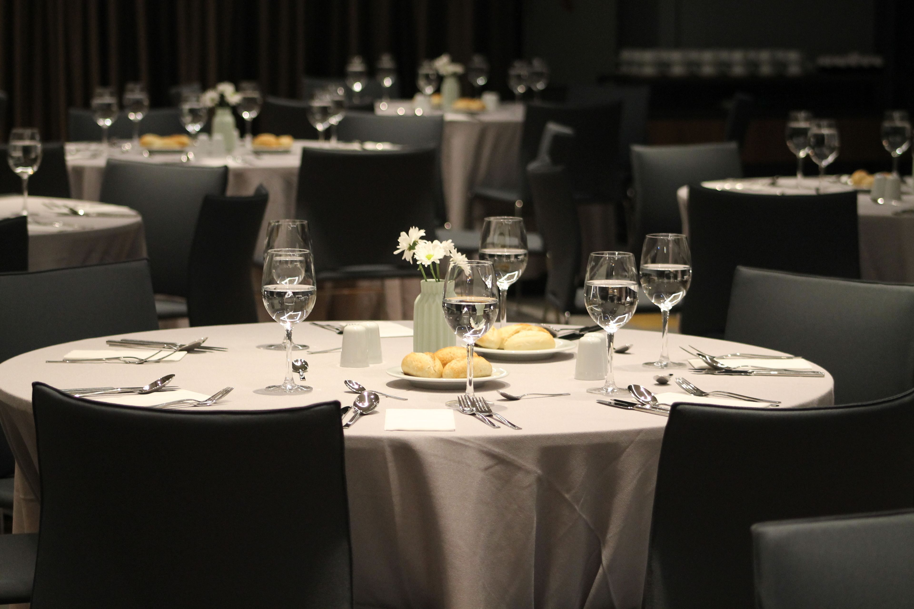 A restaurant with round tables set for dining, each with plates, cutlery, glasses, and a vase with flowers.