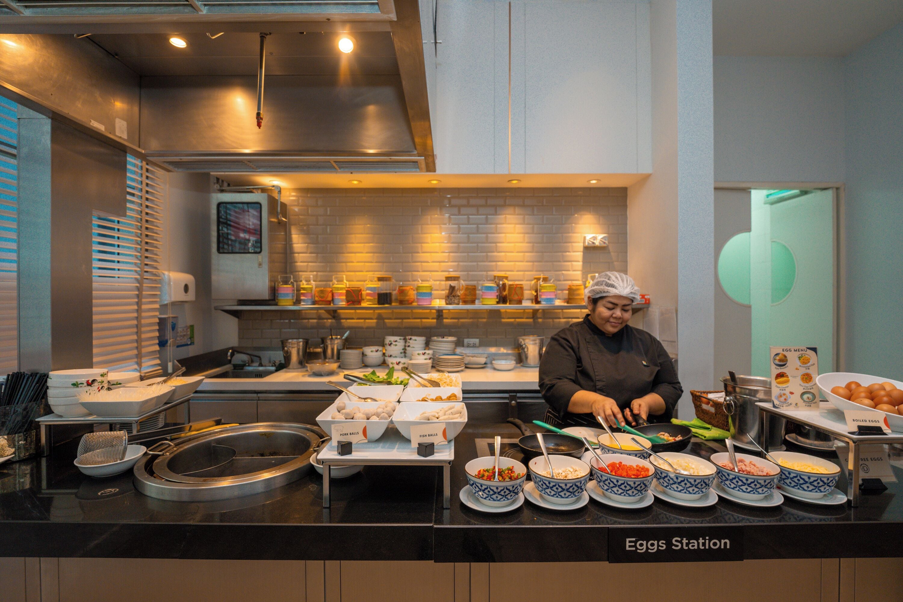 Montaje de bufé con distintas estaciones de comida, incluyendo una estación de huevos, en un ambiente de cocina moderno.