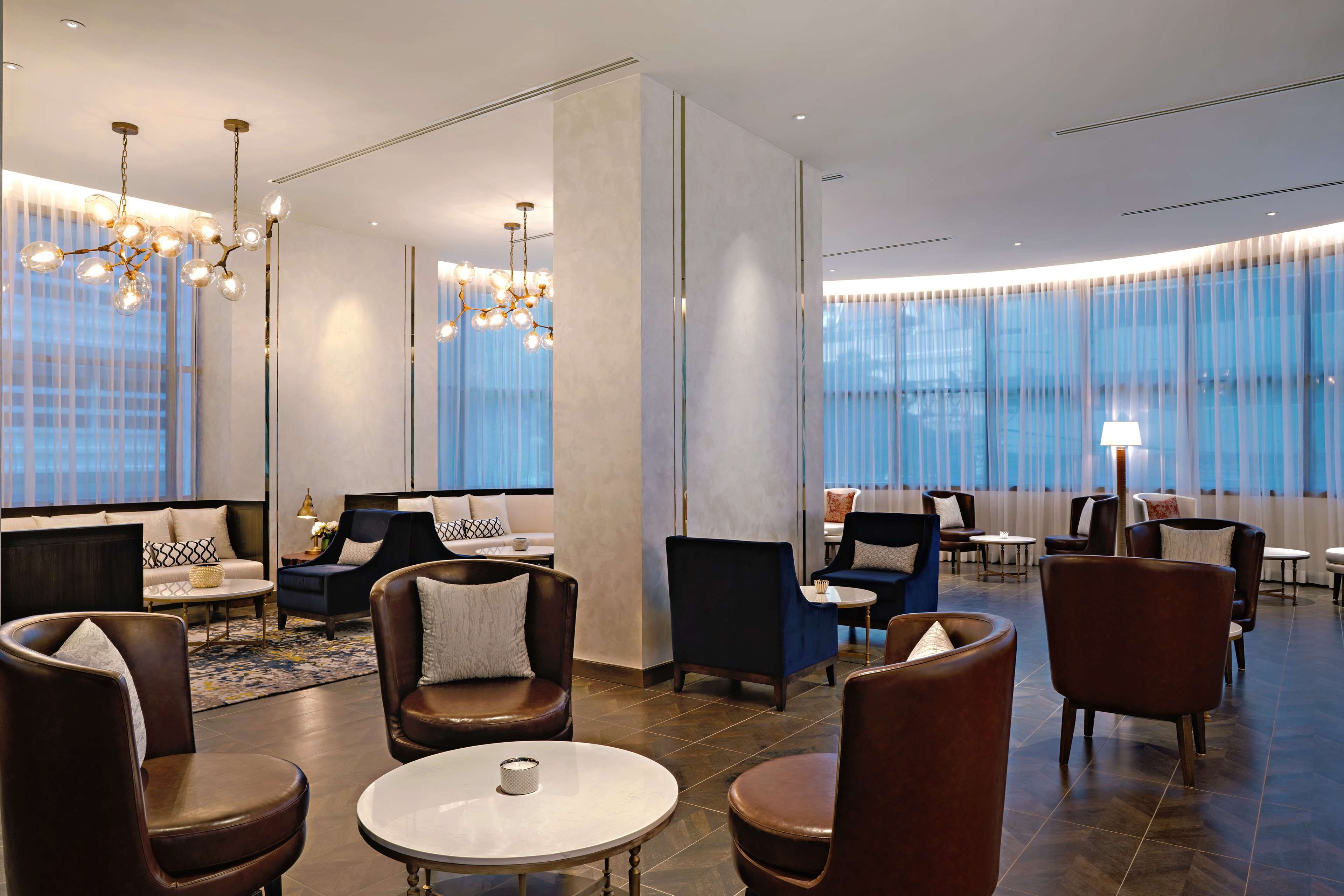 A modern hotel lobby with leather seating, a chandelier, and large windows.
