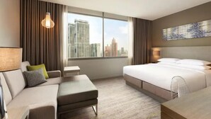 Habitación de hotel moderna con una cama grande, un sofá, una mesita y vistas a la ciudad a través de la ventana.